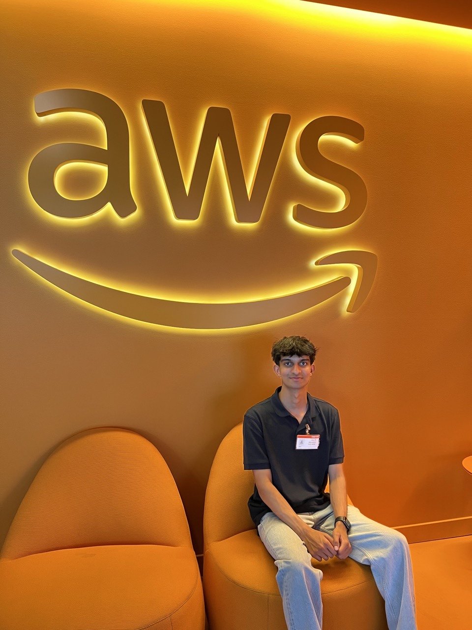 Jason seated beneath a glowing AWS logo on an orange wall.