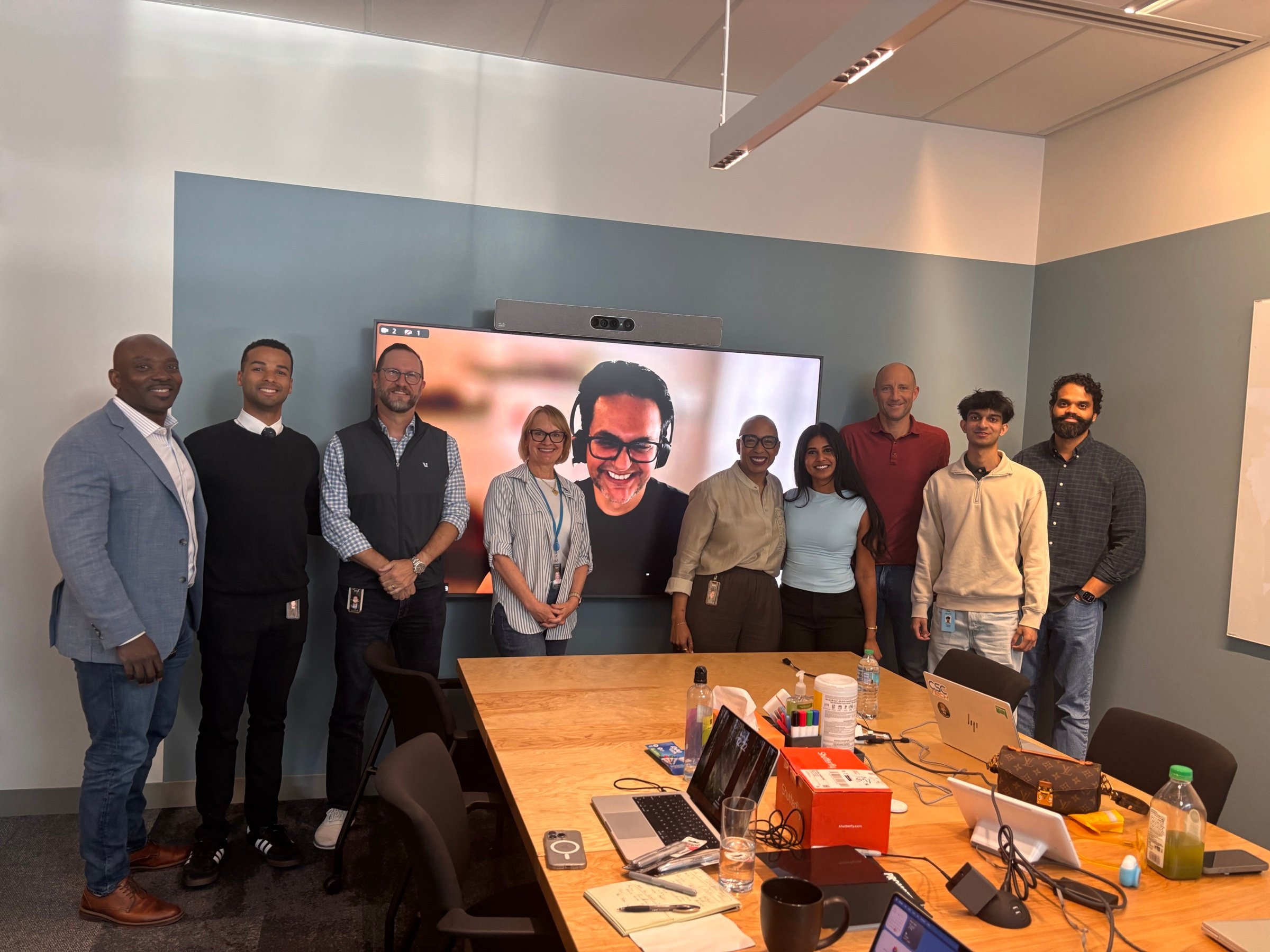 Jason with AWS senior leaders and colleagues in a conference room, one joining on the screen behind them.