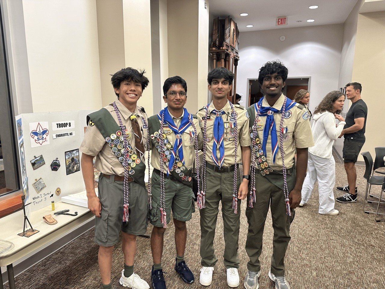 Jason and three fellow Eagle Scouts in uniform with sashes beside a Troop 8 display.