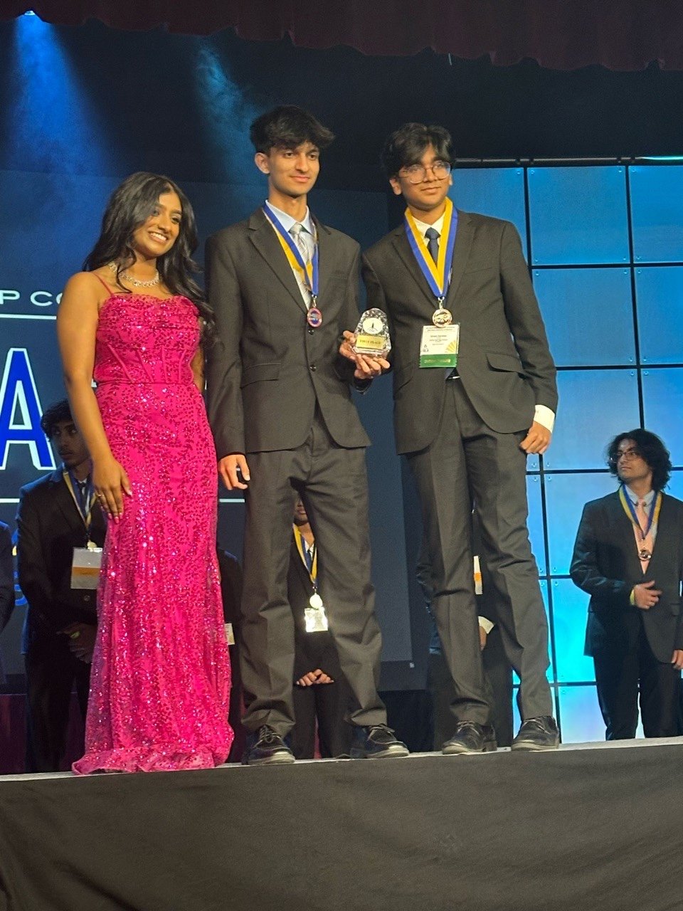 Jason and his teammate on the FBLA North Carolina awards stage wearing medals and holding a trophy.