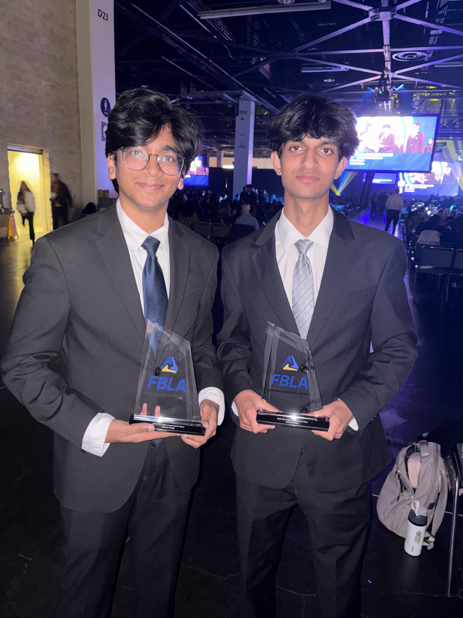 Jason and his teammate in suits, each holding an FBLA trophy in the convention hall.