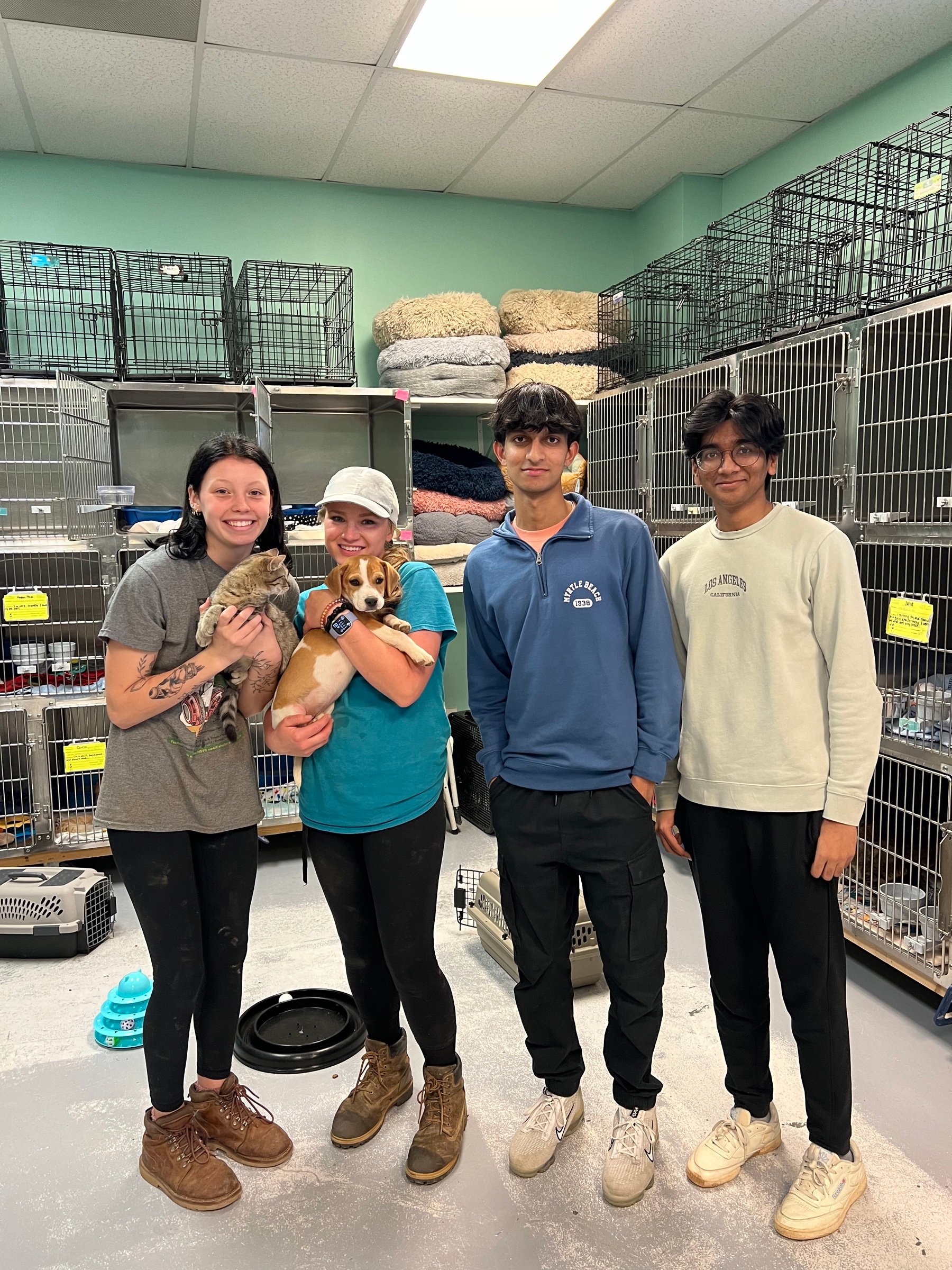 Jason, his teammate and two shelter staff holding a kitten and a puppy among the shelter's crates.