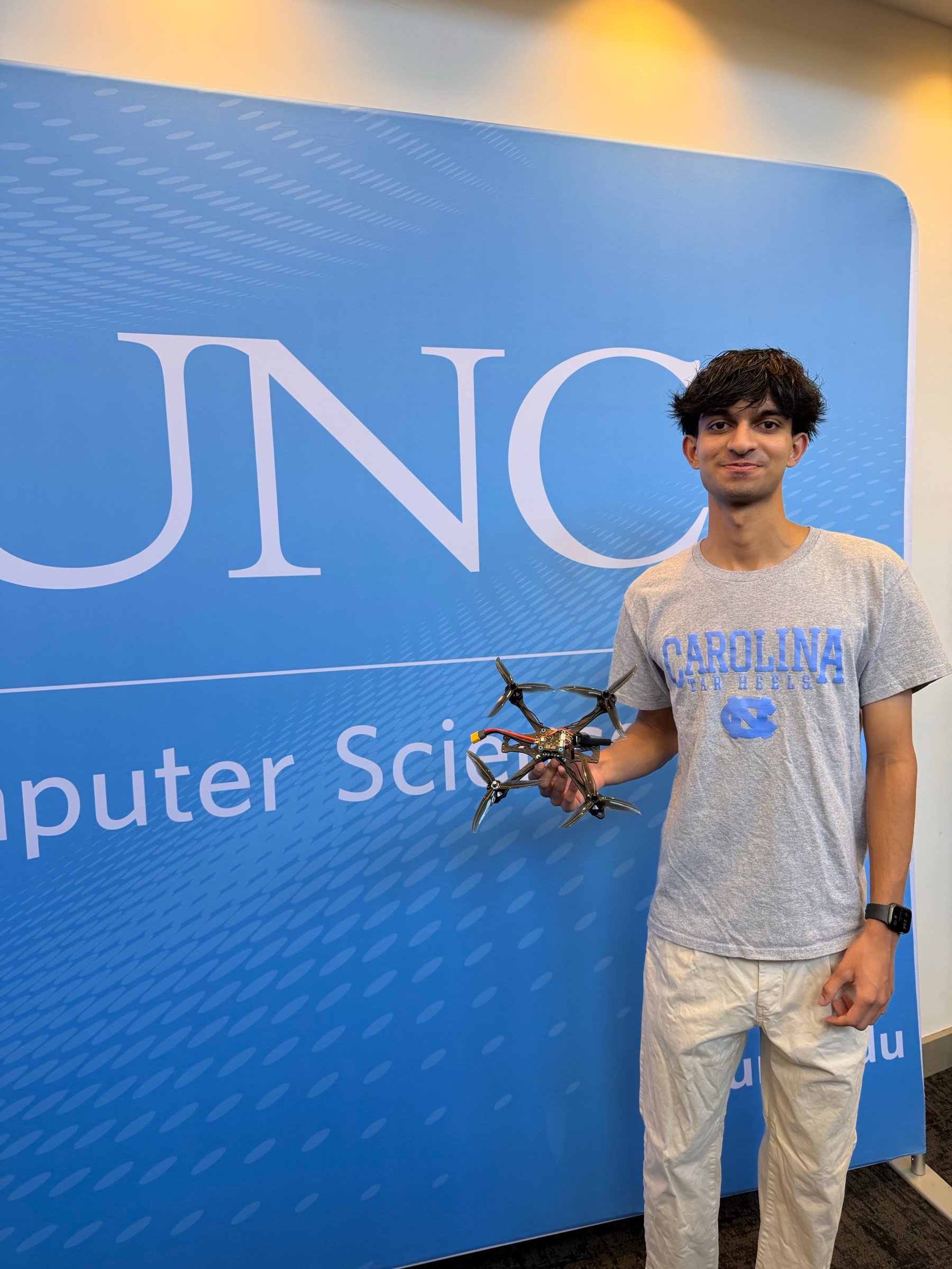 Jason holding a quadcopter drone in front of a UNC Computer Science backdrop.
