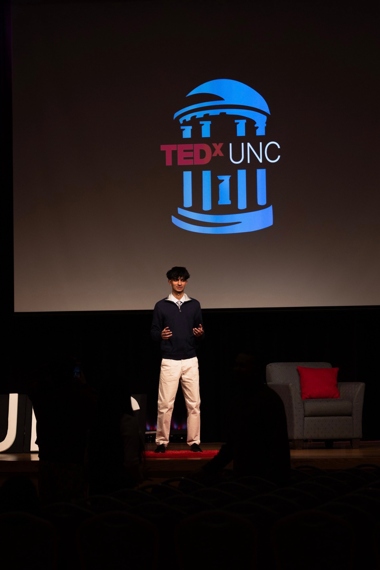 Jason speaking on stage at TEDxUNC, with the TEDxUNC logo on the screen behind him.